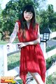 Standing against fence wearing red dress long hair over her shoulders